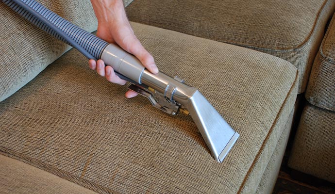 Person using a vacuum cleaner on upholstered furniture.