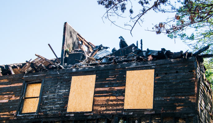 windows and doors of a fire burnt house are boarded up with plywood